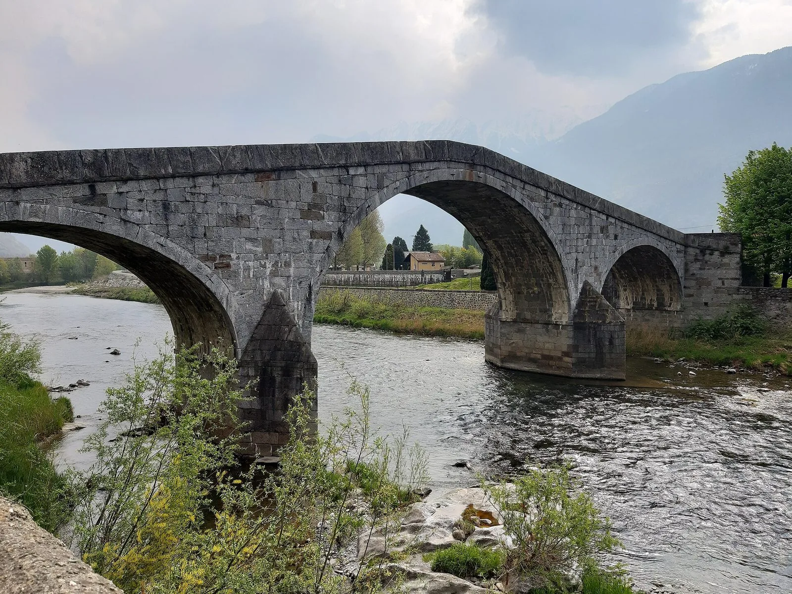 Il Ponte di Ganda a Morbegno, antico ponte in pietra a più arcate sul fiume Adda, con le montagne della Valtellina avvolte dalle nuvole sullo sfondo