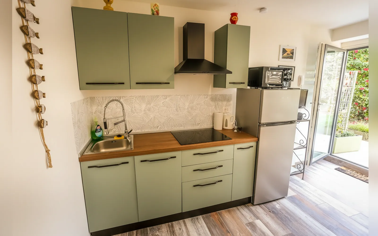 La cucina verde salvia con il piano a induzione e il frigorifero, accanto alla portafinestra