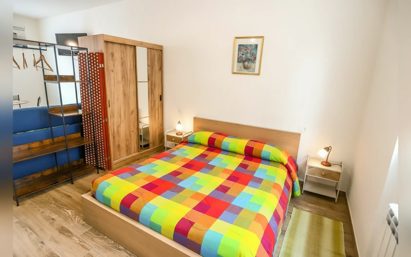 Il letto con il copriletto a quadri colorati e l’armadio in legno
